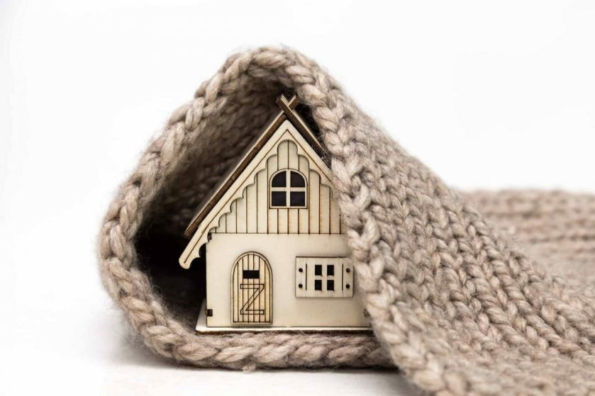 toy wooden house wrapped in a warm knitted scarf on a white background
